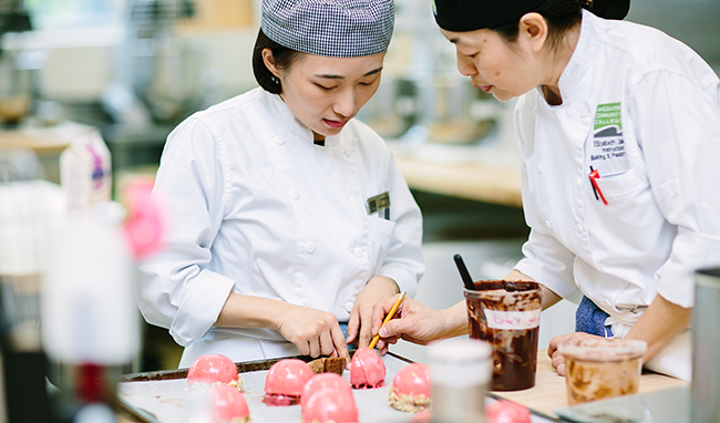 A ϲ̳ baking instructor and student look over pink pastries